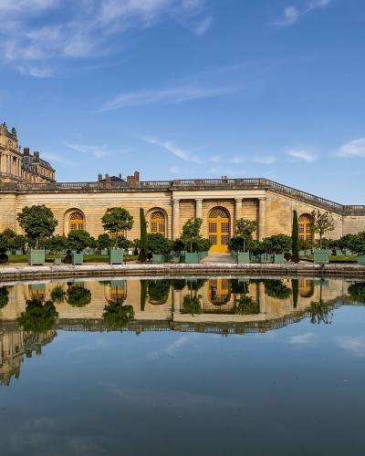 A panoramic view of the Palace of Versailles reflected in the Grand Canal on a sunny day.