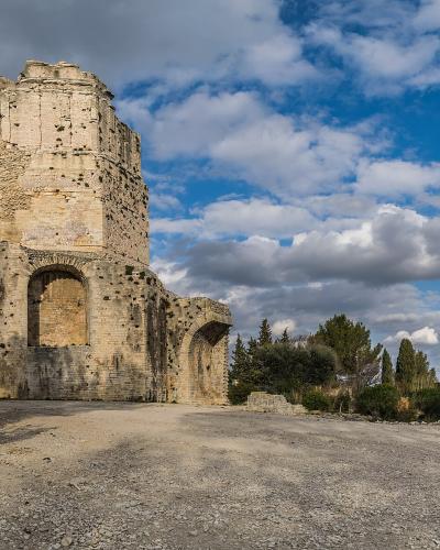 A low-angle photograph of the weathered, octagonal stone ruins of the Tour Magne tower under a partly cloudy blue sky, with gravel ground and surrounding trees.