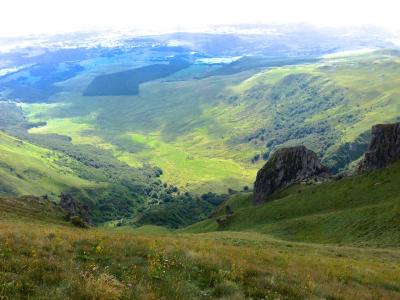 A high-angle landscape view of rolling green hills, rocky outcrops, and distant valleys under a bright sky, with no visible signage or man-made structures identifying the location.
