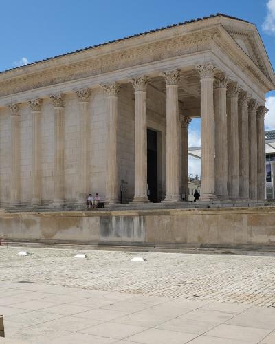 The image shows the ancient Roman temple known as the Maison Carrée in Nîmes, France, with its distinctive Corinthian columns and pediment, and the modern glass-fronted Carré d'Art museum building is visible in the background to the right.