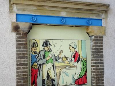 A framed vintage illustration depicting a scene with a soldier and a woman serving coffee, mounted on an exterior wall under a stone and blue metal lintel.
