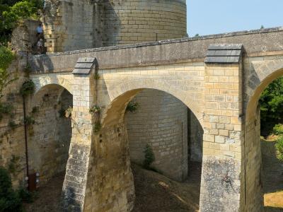 A stone bridge with multiple arches in the foreground and a large cylindrical stone tower (part of the Chinon Castle fortifications) in the background.