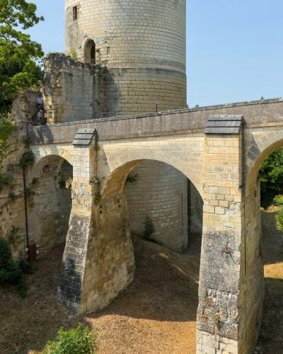 A stone bridge with multiple arches in the foreground and a large cylindrical stone tower (part of the Chinon Castle fortifications) in the background.