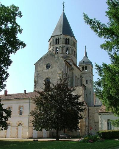 A low-angle photograph of a tall, octagonal stone bell tower with Romanesque arched windows and a pyramidal roof topped by a weather vane.