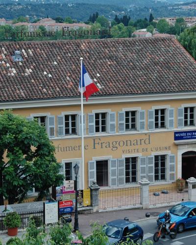 A yellow building with a tiled roof, French flag, and signage reading "Parfumerie Fragonard" and "Musée du Parfum" in Grasse, France.