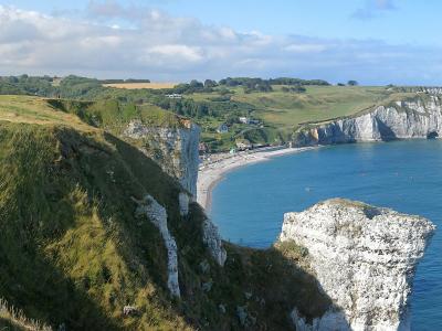 A panoramic view of the Alabaster Coast in Normandy, featuring the white chalk cliffs, the natural arch and needle rock formations of Étretat, and the Notre-Dame-de-la-Garde chapel on the cliff edge.