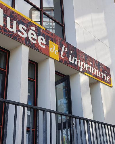 The image shows the exterior facade of a building with a large sign reading "Musée de l'imprimerie" and a smaller sign indicating "Entrée" (Entrance).