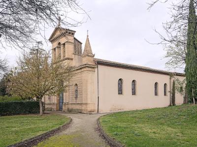 A beige stone church with a bell tower and spire, set in a grassy area with trees and a gravel path leading to the entrance.