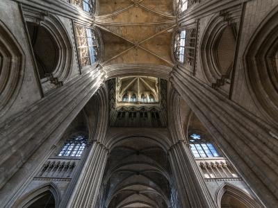 A low-angle interior photograph looking up at the stone vaulted ceilings, clustered columns, and clerestory windows of a large Gothic cathedral.