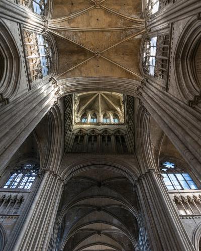 A low-angle interior photograph looking up at the stone vaulted ceilings, clustered columns, and clerestory windows of a large Gothic cathedral.