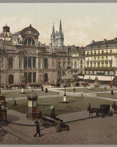 A vintage colorized photograph of a large European city square featuring a grand ornate building (likely a theater or opera house) on the left, horse-drawn carriages and an early tram in the foreground, with a cathedral spire visible in the backgr