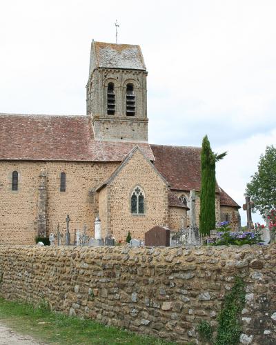 A stone church with a tiled roof and bell tower, situated behind a low stone wall that encloses a cemetery with visible crosses and headstones.