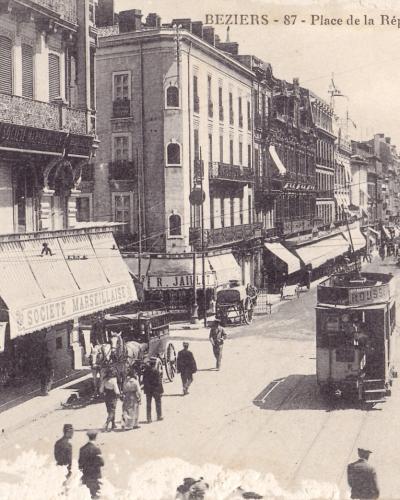 A vintage sepia photograph showing a street scene in Béziers, France, featuring a tram, horse-drawn carriages, pedestrians, and buildings with awnings, with the caption "BEZIERS - 87 - Place de la République - Allées Paul Riquet" at the top.