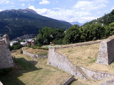 A view of stone fortification walls and grassy ramparts with a playground and mountainous background.