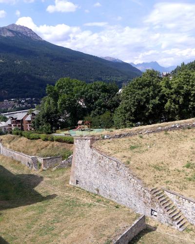 A view of stone fortification walls and grassy ramparts with a playground and mountainous background.