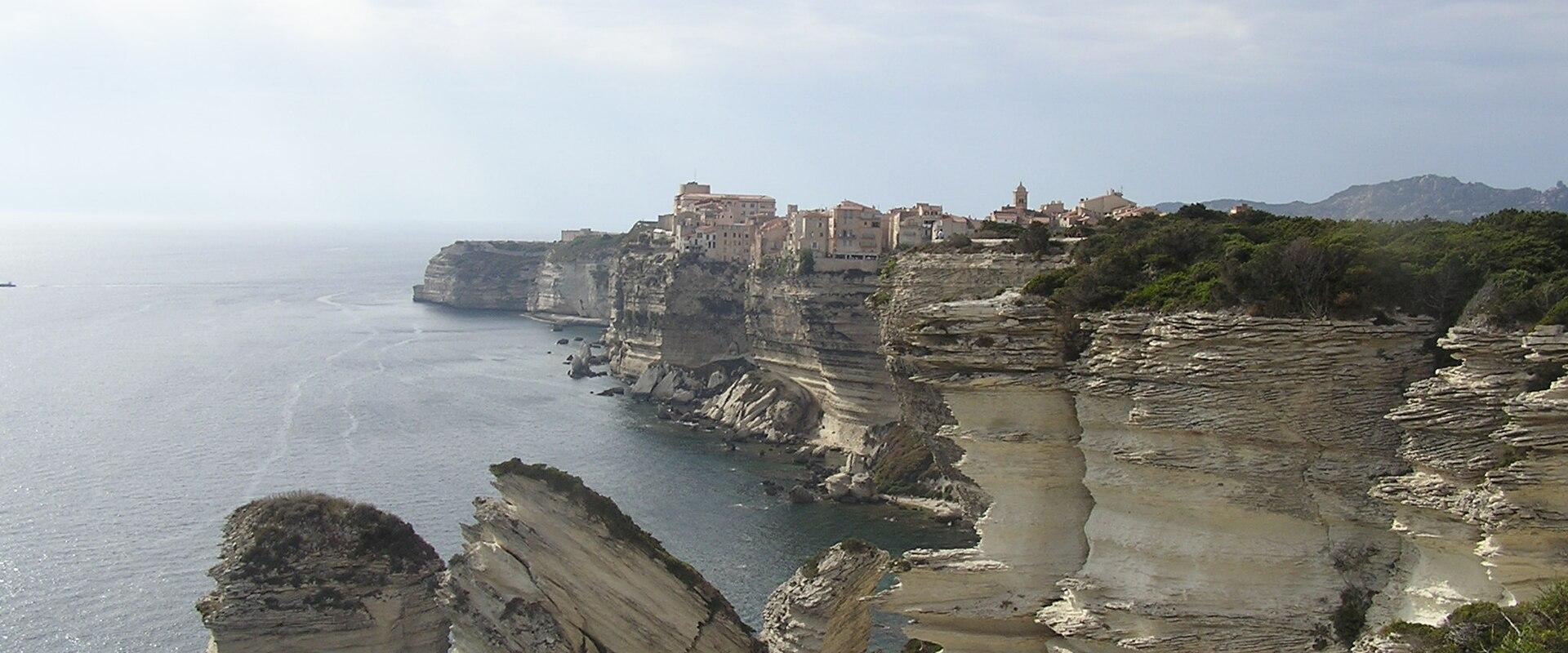 Bonifacio perched on white limestone cliffs above the sea, with the Grain de Sable rock, Corsica