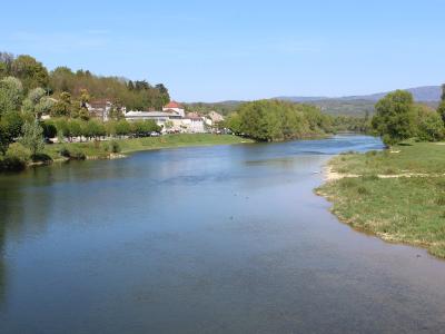 A wide river flowing through a green valley with a town on the left bank and hills in the distance under a blue sky.