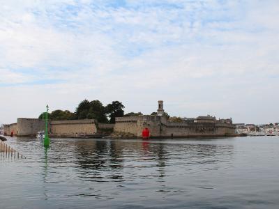 The image shows a fortified stone enclosure (the Ville Close) on a small island, connected to the mainland by a bridge, with a green navigational buoy in the foreground and a church tower visible within the walls.