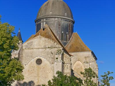 A stone church with a large grey dome and lantern tower, viewed from below through green trees against a clear blue sky.