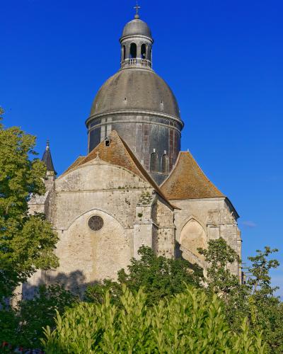 A stone church with a large grey dome and lantern tower, viewed from below through green trees against a clear blue sky.