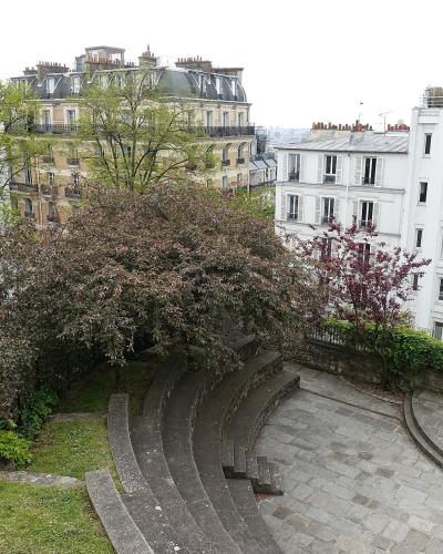 The image shows a small, semi-circular stone amphitheater or garden seating area surrounded by trees and typical Parisian apartment buildings with mansard roofs.