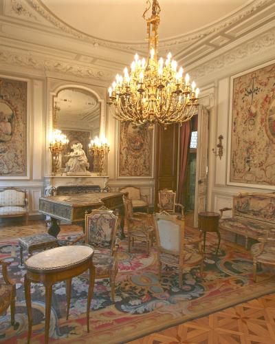 An ornate 19th-century interior room featuring a large chandelier, gilded furniture, tapestries on the walls, a grand piano, and parquet flooring, identified as the music salon of the Musée Grobet-Labadié.
