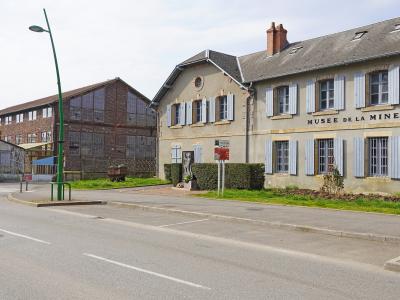 The image shows the exterior of a building with "MUSEE DE LA MINE" signage, located in La Machine, France, featuring a brick industrial structure and a beige building with blue shutters.