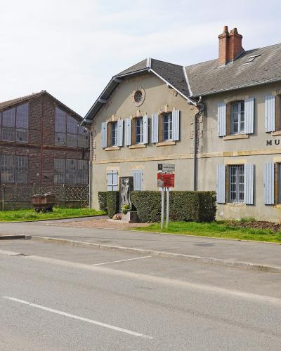 The image shows the exterior of a building with "MUSEE DE LA MINE" signage, located in La Machine, France, featuring a brick industrial structure and a beige building with blue shutters.