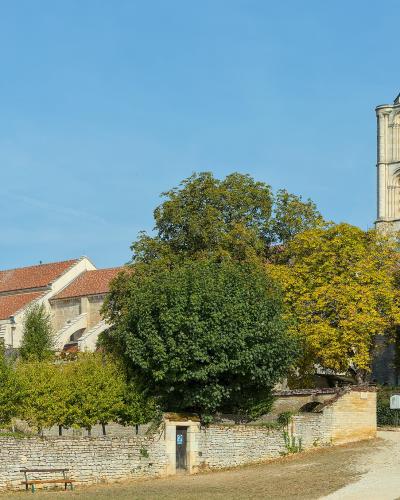 A large Romanesque basilica with two prominent square towers and a red-tiled roof, viewed from a distance across a grassy area with trees and a low stone wall.