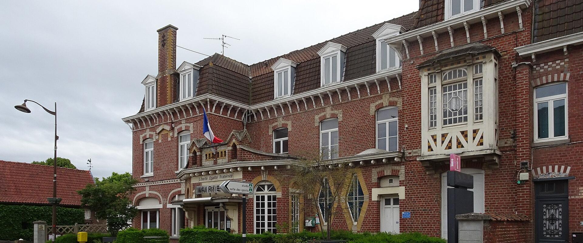 A red-brick municipal building (mairie) with a French flag, signage reading "Mairie" and "Forest-sur-Marque," set on a street corner with sidewalks, bollards, and flowerbeds.