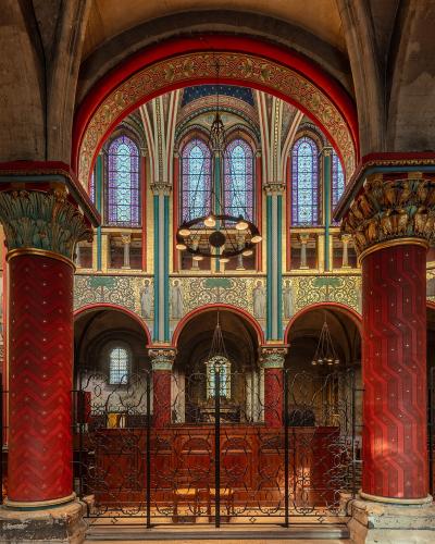 The image shows the interior of a church featuring distinctive red zigzag-patterned columns, colorful frescoes, and stained glass windows, with a visible Latin inscription on the wall reading "HIC FUIT ECCLESIA SANCTI GERMANI" (Here was the Church