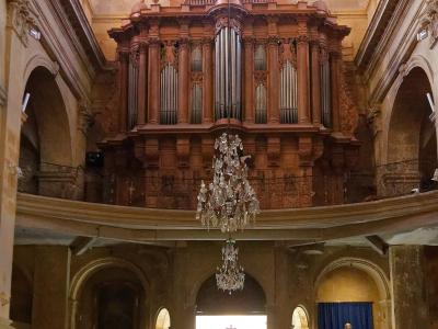 The interior of a church featuring a large wooden pipe organ on a balcony, stone arches, and pews.