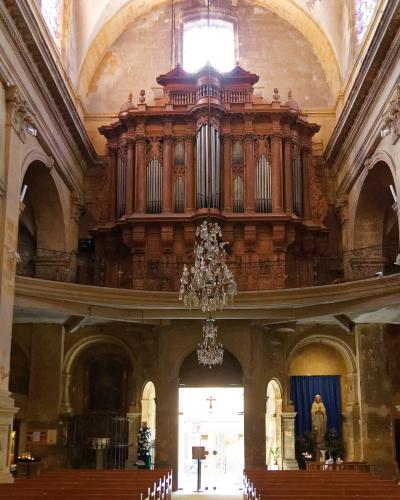 The interior of a church featuring a large wooden pipe organ on a balcony, stone arches, and pews.