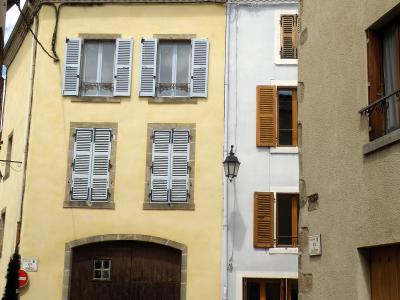 A narrow street scene featuring a yellow building with white shutters and a large wooden garage door, alongside a white building with brown shutters, under a blue sky.