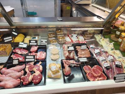 A close-up view of a butcher's refrigerated display case filled with various raw meats, including duck legs, sausages, and terrines, with price tags written in French.
