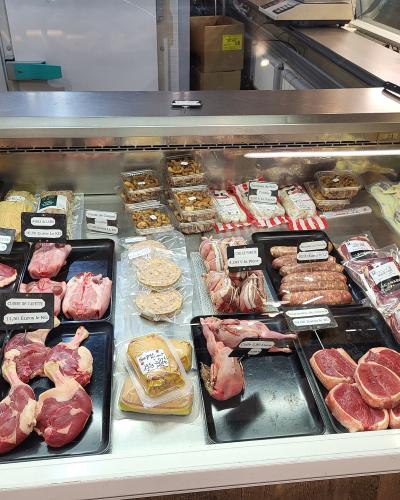 A close-up view of a butcher's refrigerated display case filled with various raw meats, including duck legs, sausages, and terrines, with price tags written in French.