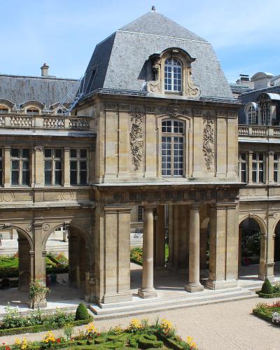 A black-and-white photograph of a formal courtyard garden with ornate gravel patterns, flanked by Renaissance-style buildings featuring arched colonnades and classical facades, with a watermark in the lower-left corner reading "PALIER" and "PARIS"