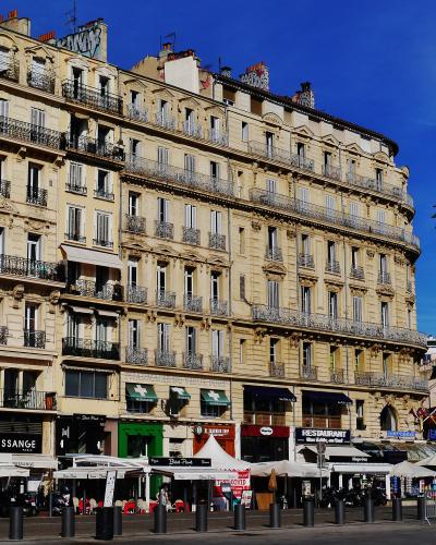 A street-level view of a curved, multi-story beige building with wrought-iron balconies and ground-floor shops including "DESSANGE" and "RESTAURANT," adjacent to a white church facade under a clear blue sky.