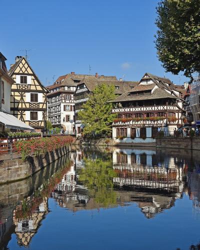 A scenic view of the Lauch River in the Petite France district of Strasbourg, France, featuring traditional half-timbered houses including the prominent Maison des Tanneurs on the right bank.