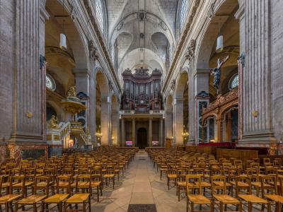 The image shows the interior nave of a large, historic church with tall fluted columns, arched ceilings, rows of wooden chairs, and stained-glass windows; no visible signage or text is present.