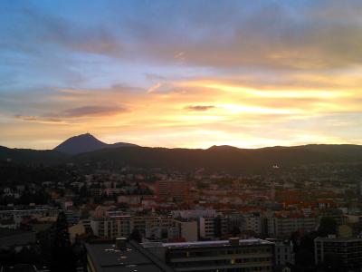 A sunset view over a city with a prominent conical mountain silhouette in the distance, featuring a tower or structure on its peak; no visible signage or text.