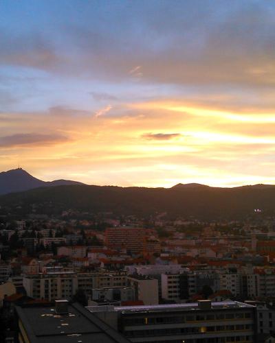 A sunset view over a city with a prominent conical mountain silhouette in the distance, featuring a tower or structure on its peak; no visible signage or text.