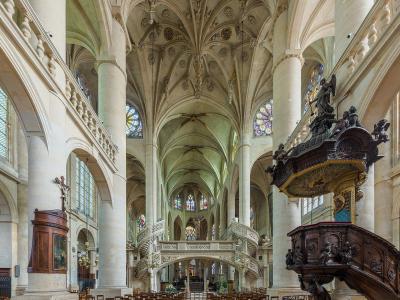 The image shows the interior nave of a large Gothic-style church featuring a prominent, ornate wooden pulpit on the right, a stone double staircase leading to a tribune, and a vaulted ceiling with decorative bosses.
