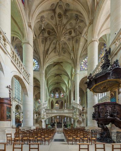The image shows the interior nave of a large Gothic-style church featuring a prominent, ornate wooden pulpit on the right, a stone double staircase leading to a tribune, and a vaulted ceiling with decorative bosses.