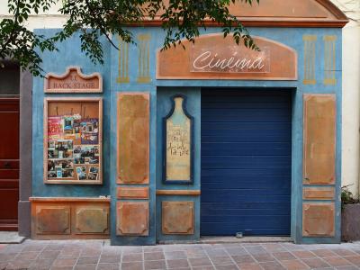 A blue and terracotta-colored cinema facade with signage reading "Cinéma", "LE BACK-STAGE", and "LE MISTRAL", featuring a poster board and a closed blue roller shutter.