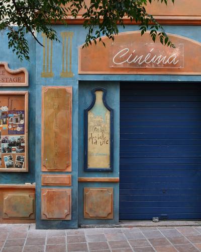 A blue and terracotta-colored cinema facade with signage reading "Cinéma", "LE BACK-STAGE", and "LE MISTRAL", featuring a poster board and a closed blue roller shutter.