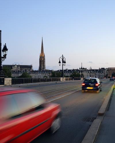 A view from a bridge at dusk showing tram tracks, a dedicated bike lane, ornate street lamps, and a prominent Gothic church spire in the background.