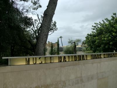 A low stone wall with large, gold-colored metal letters spelling "MUSEE NATIONAL MARC CHAGALL" set against a backdrop of trees and a cloudy sky.