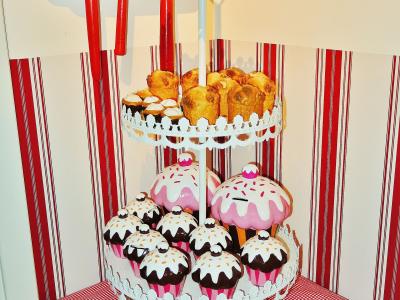 A display of oversized gingerbread and cupcake models on a white tiered stand, with a red wooden shelf above, set against a red-and-white striped wall.