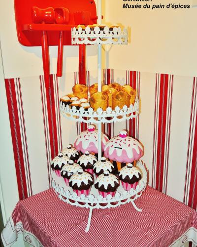 A display of oversized gingerbread and cupcake models on a white tiered stand, with a red wooden shelf above, set against a red-and-white striped wall.
